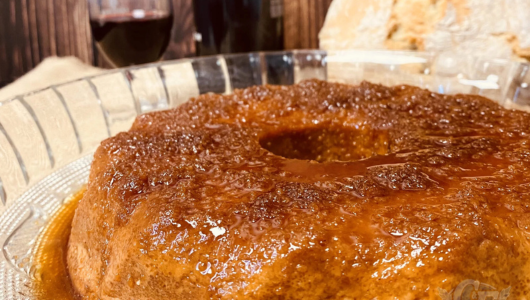 Close-up of a glazed bundt cake on a glass plate with wine glass in background.