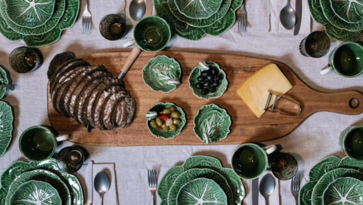 Table set with green leaf plates, bread, cheese, and olives on a wooden serving board.