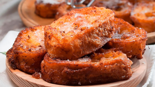 A plate of golden-brown French toast slices sprinkled with sugar.