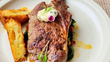 Grilled steak with herb butter, served with potato wedges on a white plate.