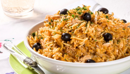 Bowl of rice with black olives and herbs, placed on a table with a fork beside it.