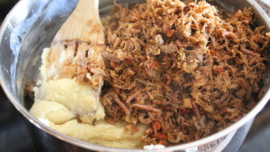 Shredded meat with mashed potatoes in a pot, stirred by a wooden spatula.