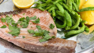 Grilled tuna steak with parsley, green beans, lemon wedge, and potatoes on a silver plate.