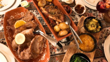Plates of meats, potatoes, and side dishes on a decorated table with utensils.
