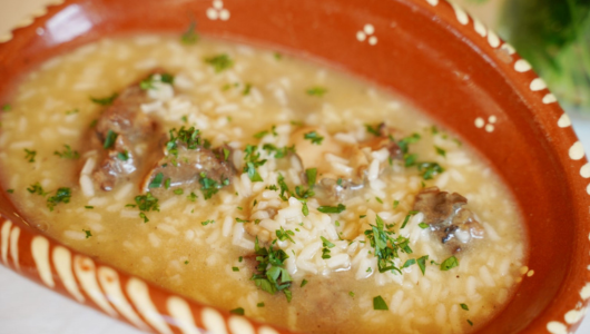 Ceramic dish with rice soup, meat, and parsley garnish.