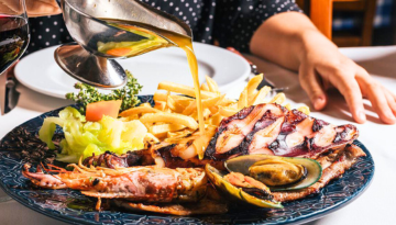 Seafood platter with sauce, fries, vegetables, and grilled items on a plate.