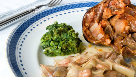 Plate with cooked greens, meat, beans, and cutlery on the side.
