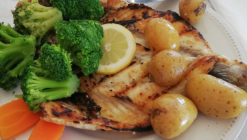 Grilled fish with lemon, potatoes, broccoli, and carrots on a plate.