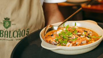 Person serving a dish of stew garnished with herbs and carrots in a restaurant setting.