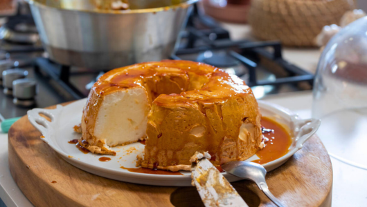 Partially sliced caramel pudding on a plate with a serving knife.