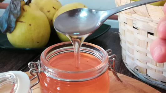 Spoon dripping syrup into an open jar, with yellow fruits in the background.