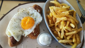 Sausage with sunny-side-up egg, fries in a bowl, and a small dish of sauce on a plate.
