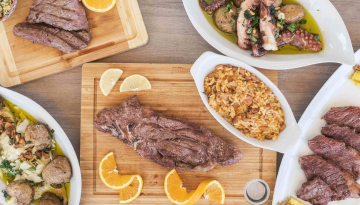 Assorted grilled meats and seafood with rice and lemon slices on platters.