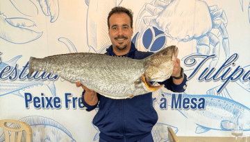 Person holding large fish in front of seafood-themed mural.