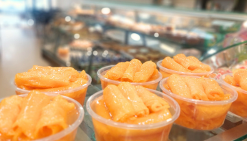 Plastic cups filled with orange rolled pastries on a counter in a bakery.