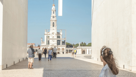 People walking towards a church with a tall clock tower on a sunny day.