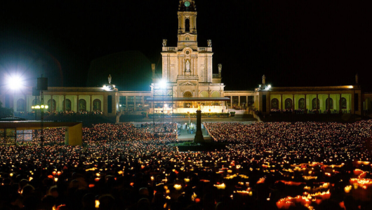 Large crowd holding candles in front of a lit-up cathedral at night.