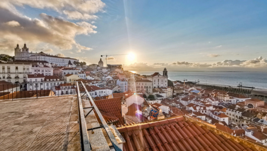 Rooftop view of a coastal city at sunset with historic buildings and ocean.