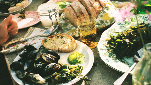 Outdoor meal with mussels, bread, salad, and a drink on a table.