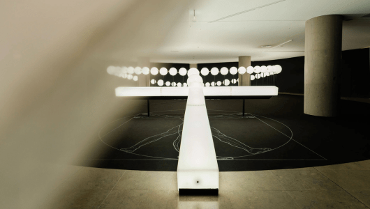 Abstract installation with illuminated linear structure and circular lights on a dark floor.