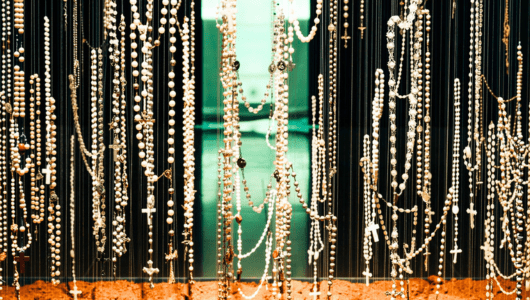 Numerous rosaries with beads and crosses hang vertically on strings.