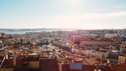 Cityscape view with buildings and a river under a sunny blue sky.