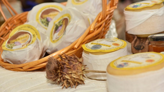 Basket of cheese with labels, surrounded by honey jars and a dried artichoke.