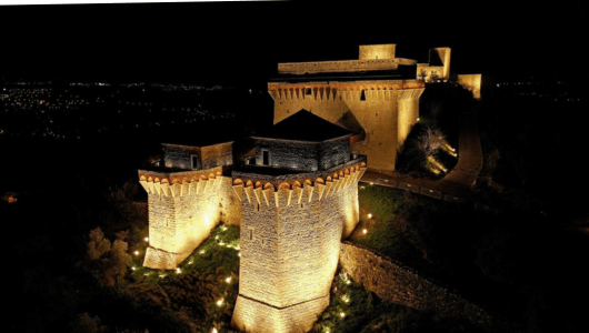 Illuminated stone castle at night with towers and walls.