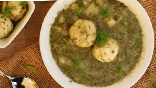 Bowl of soup with eggs and herbs on a wooden table.