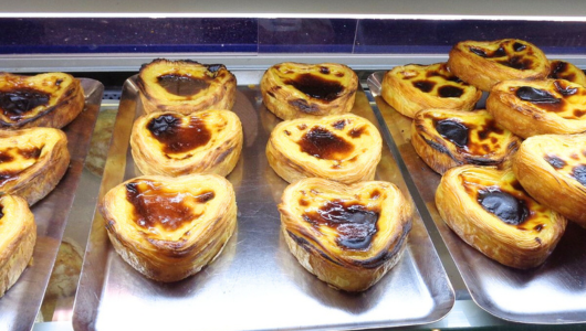 Trays of custard tarts with golden tops in a display case.