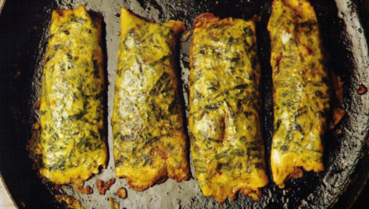 Four cooked fish fillets with herbs in a skillet.