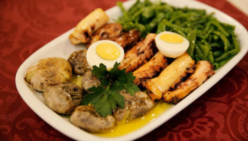 Plate with grilled vegetables, hard-boiled eggs, and green beans on a red tablecloth.