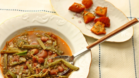Bowl with bean stew next to a plate with roasted orange vegetables.