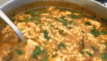 Noodle soup with herbs and chicken in a pot with a metal spoon.