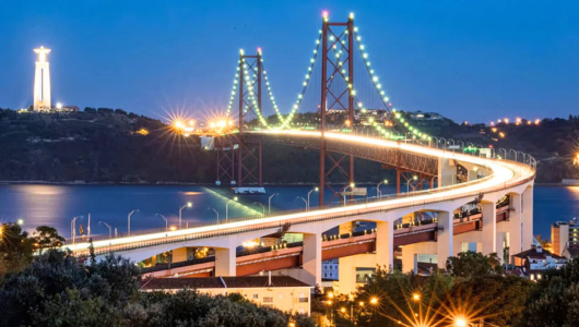 Illuminated bridge with distant statue and city lights at dusk.