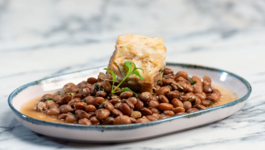 Beans with a piece of meat garnished with parsley on a plate.