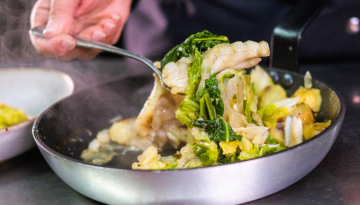 Person scooping sautéed vegetables from a pan with a spoon.