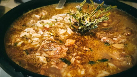 Soup with meat, grains, herbs in a black bowl.