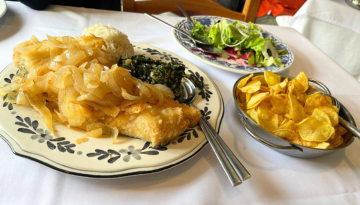 Plates with fish, onions, greens, salad, and chips on a white tablecloth.