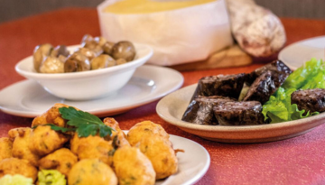 Plates of fritters, sausages on lettuce, and a wheel of cheese on a red table.
