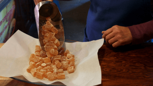 Person pours sugar-coated candies onto paper on a wooden table.