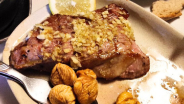 Grilled meat with garlic topping, lemon wedge, and figs on a plate.