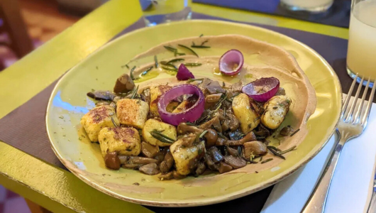 Plate of gnocchi with mushrooms, red onion, and herbs on a green plate.