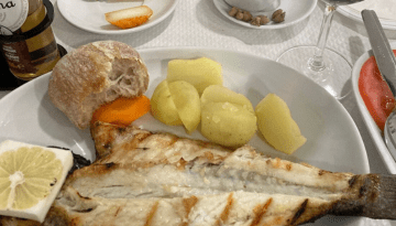 Grilled fish with potatoes and bread on a white plate.