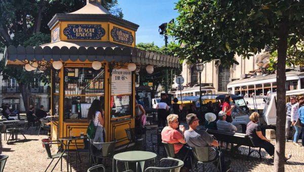 Outdoor café kiosk with people seated at tables on a sunny day.