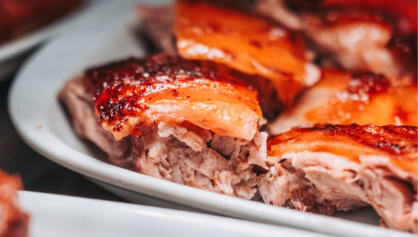 Close-up of sliced cooked meat with crispy skin on a white plate.