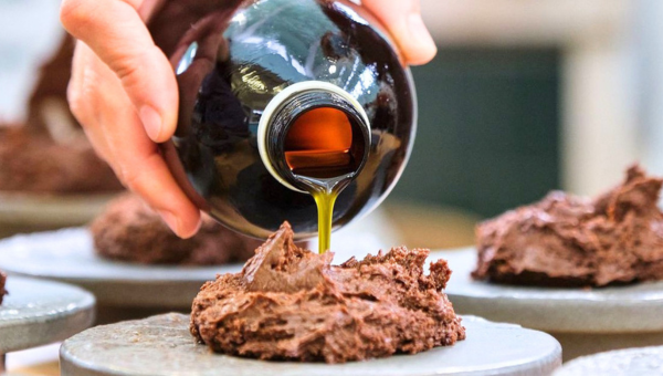 Hand pouring liquid from a bottle onto chocolate desserts.