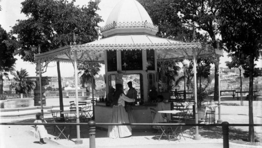Vintage photo of people at a gazebo-style outdoor café with trees and chairs.