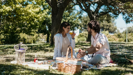 Couple enjoying a picnic on grass under trees with a basket.
