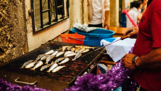 Person grilling fish on a barbecue near a stone wall.